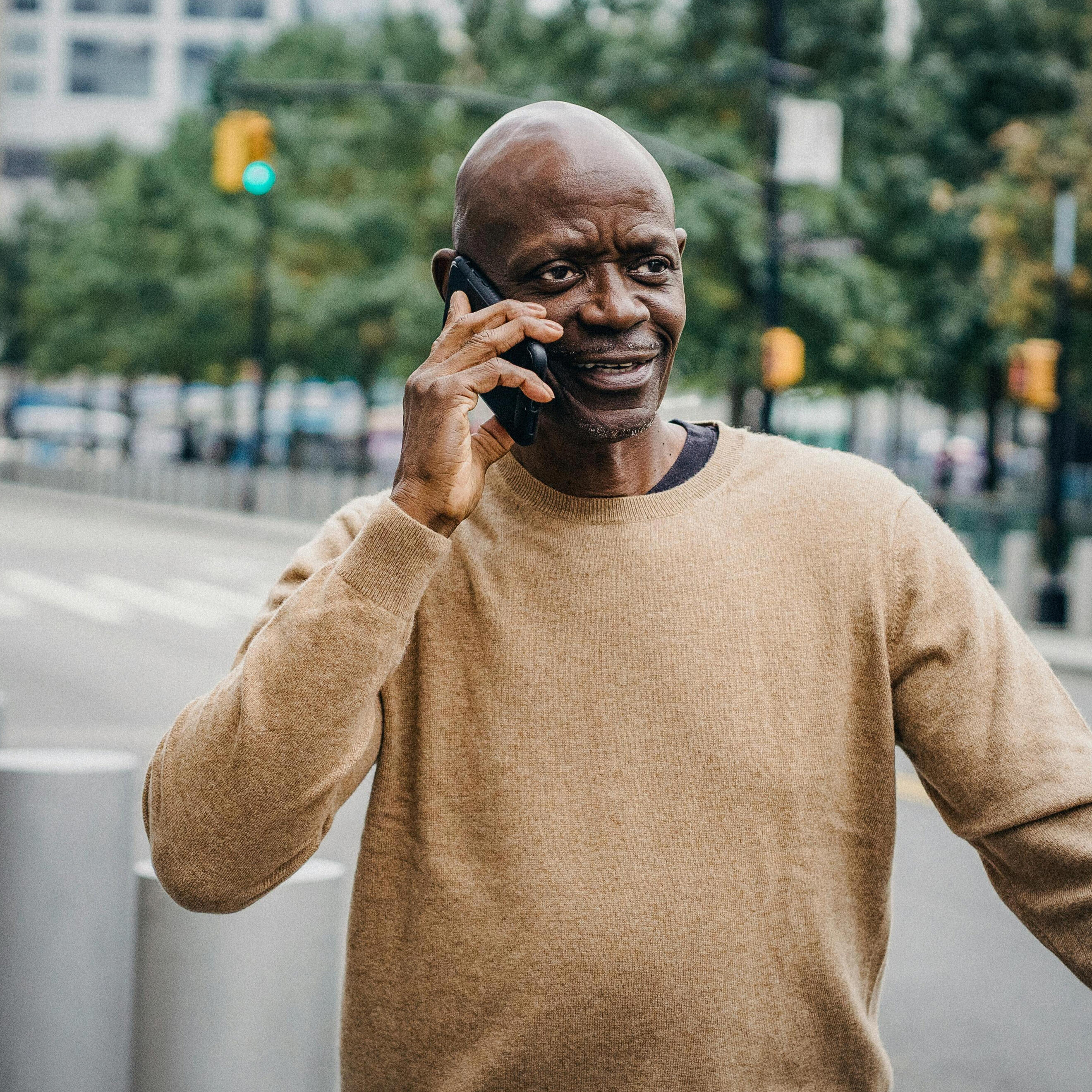 A man talking on his cellphone while standing on the sidewalk of a city street.