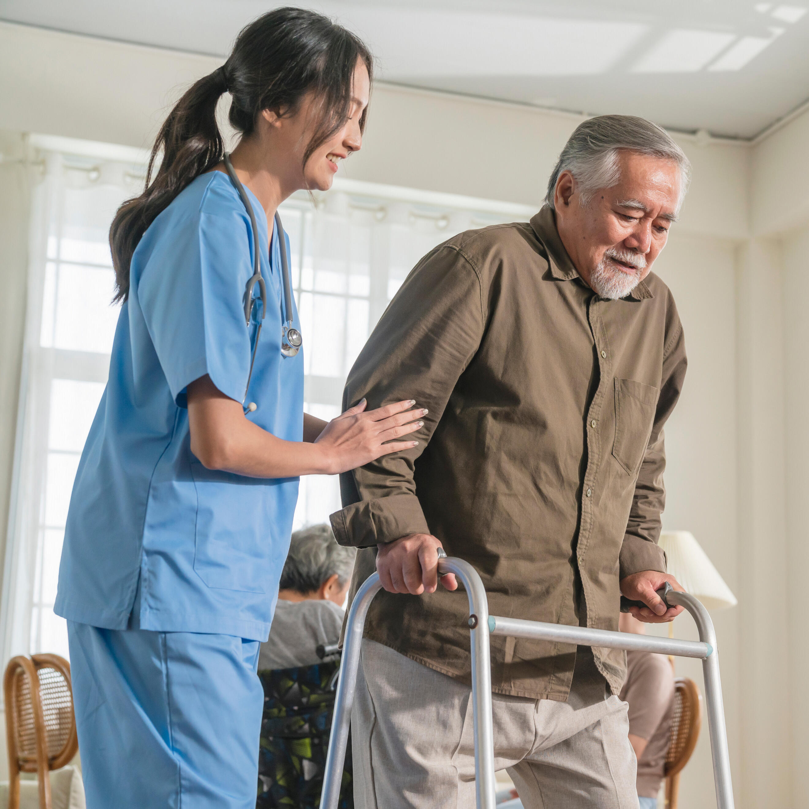 A woman in scrubs helping an older man using a walker
